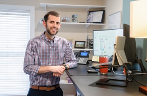 Kevin Flint, CFP®, standing smiling for photo with donor advised funds and inheritance work on his desk.